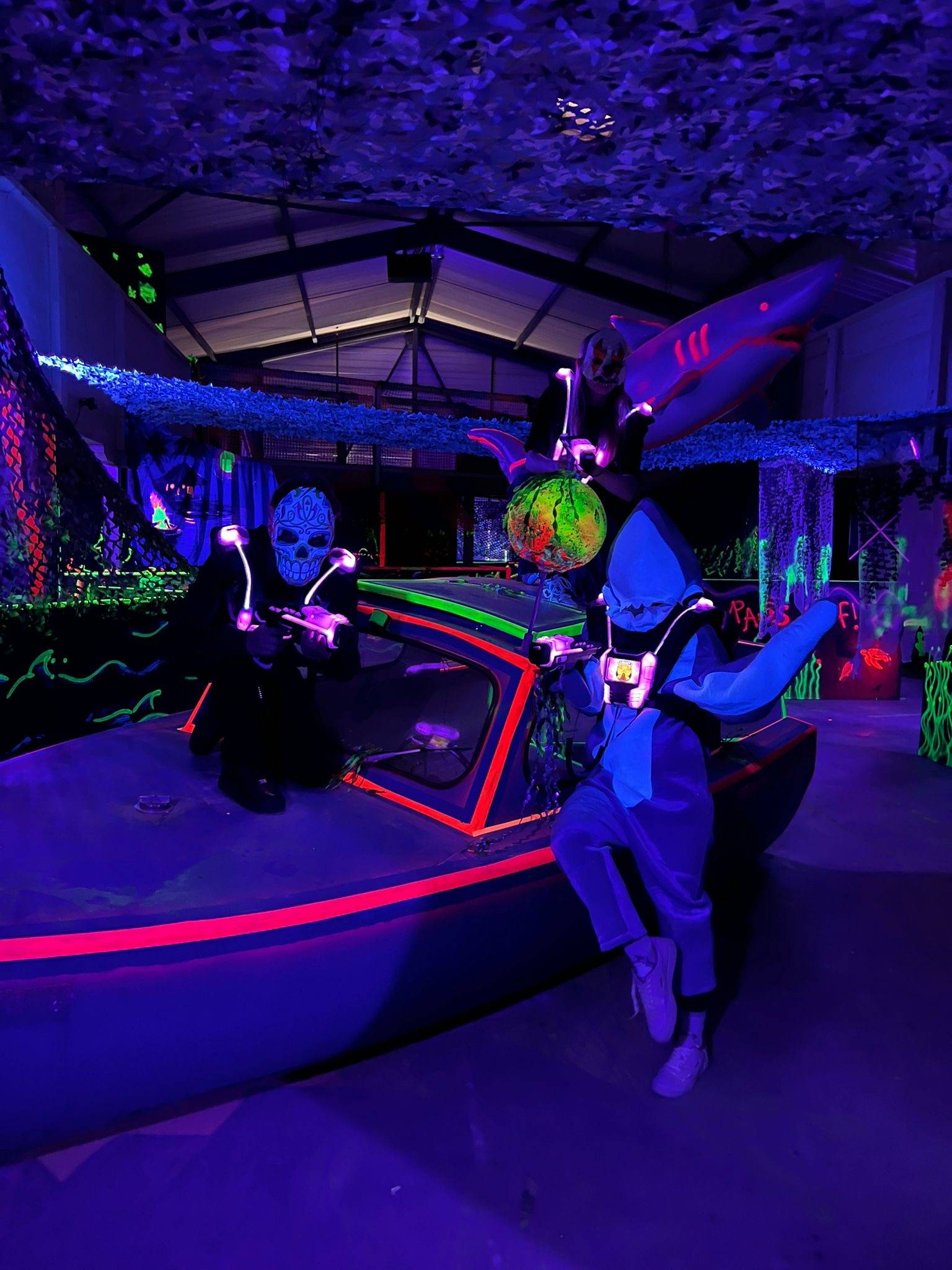 A photo of two halloween dressed players at the laser tag of Challenge Arena in Wangen, Canton Schwyz, it is in dark light with neon paint all over the walls and obstacles.  