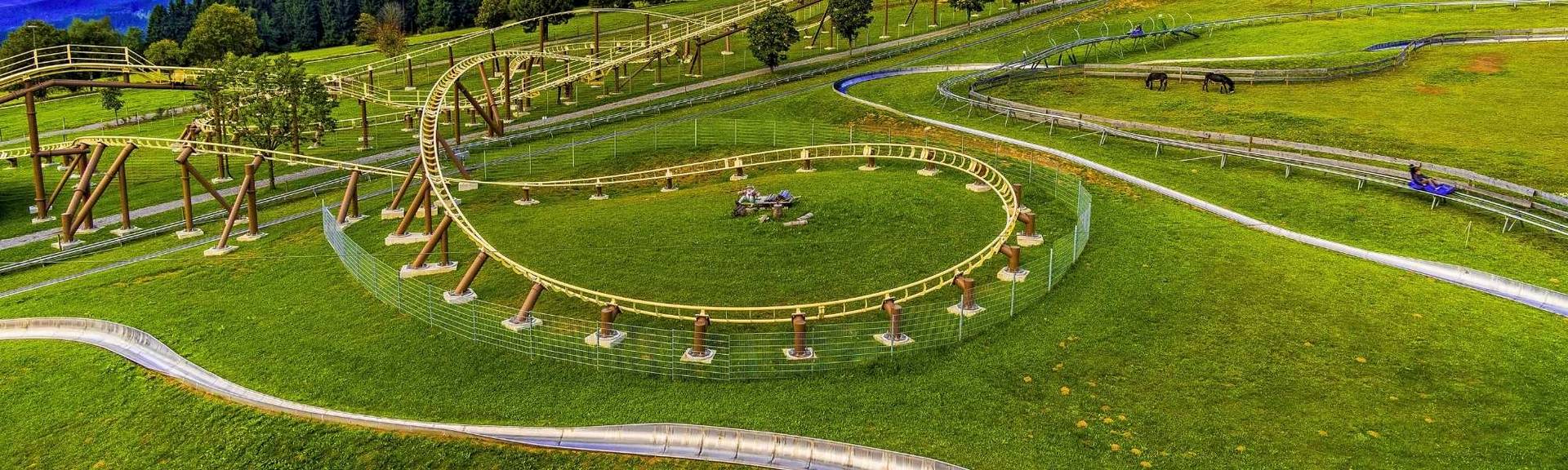 Child riding down the Brunni summer toboggan run on a winding metal track surrounded by green alpine meadows and mountain scenery.