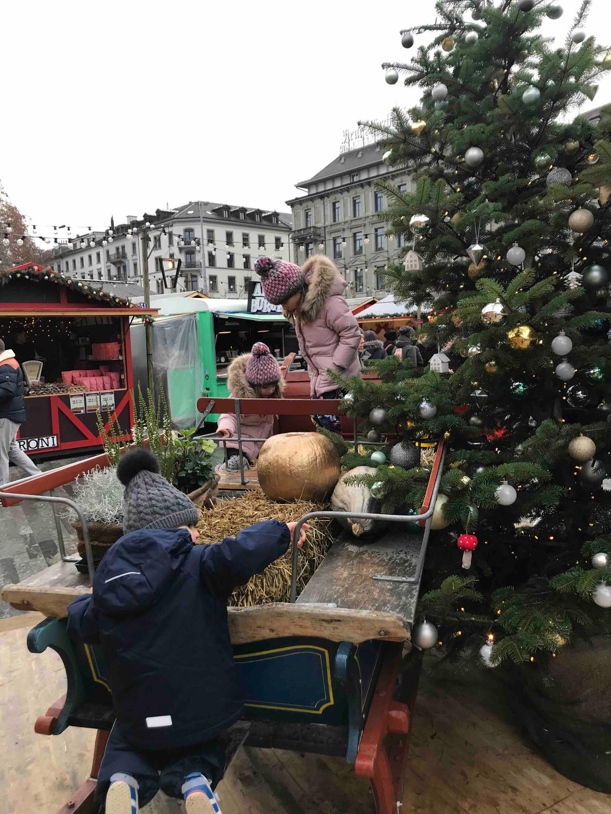 Three kids playing on a Christmas Sledge at Bellevue Christmas Market and Ice Skating Rink in Zurich