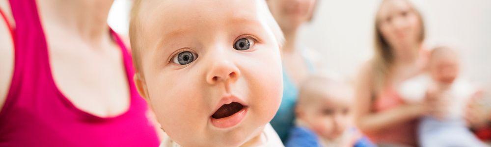 The face of a blue-eyed baby looking into the camera while his mother is holding him in a ContaKids class for movement experience in Flomotion, Zurich, Switzerland.