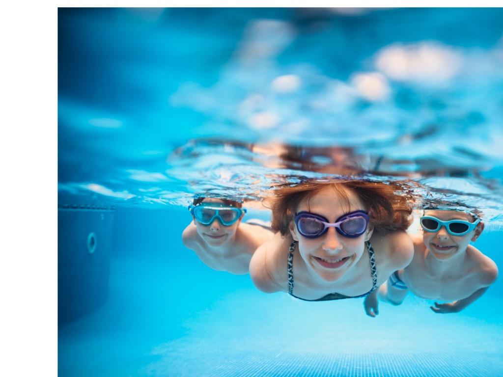 A photo of a teen girl and boy under water wearing goggles in a racing lane at the Hallenbad in Kilchberg, in Zurich