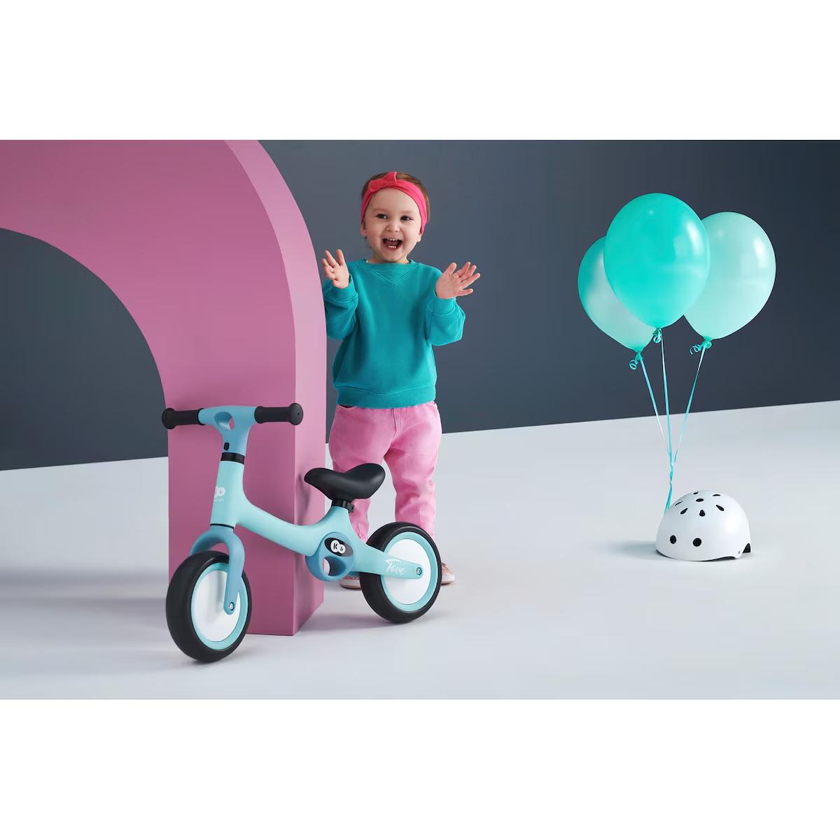 Kinderkraft TOVE Laufrad – leichtes Balance-Bike in Summer Mint, kindgerecht ab ca. 2 Jahren; Kind neben Rad und Helm.
