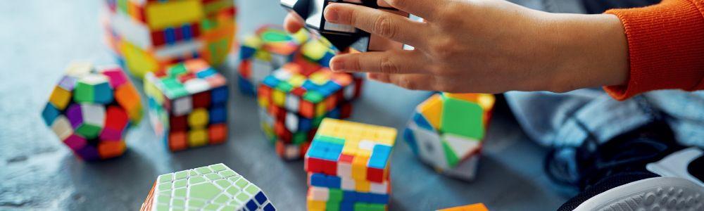 A pair of young hands holding a rubics cube and trying to solve similar 3-d puzzles.