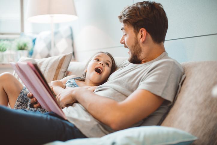 Dad and daughter reading a book together and laughing on the sofa