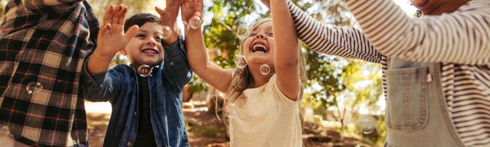 A group of pre-schoolers and young primary school age boys and girls are enjoying the forrest and blowing bubbles with their hands up in the air together, at The Outdoor Classroom near Zurich, Switzerland.