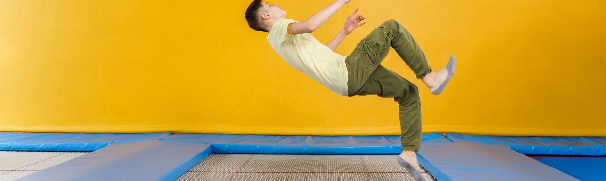 A young teen in a trampoline park is mid-air ready to land with this back on a trampoline net.  He is wearing a yeallow t-shirt and khaki pants.