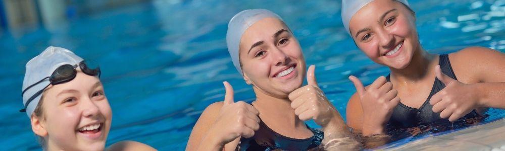 Three teen girls wearing their white swimming caps are giving a happy thumbs-up after competitive swimming in Hallenbad Uster, in Switzerland.