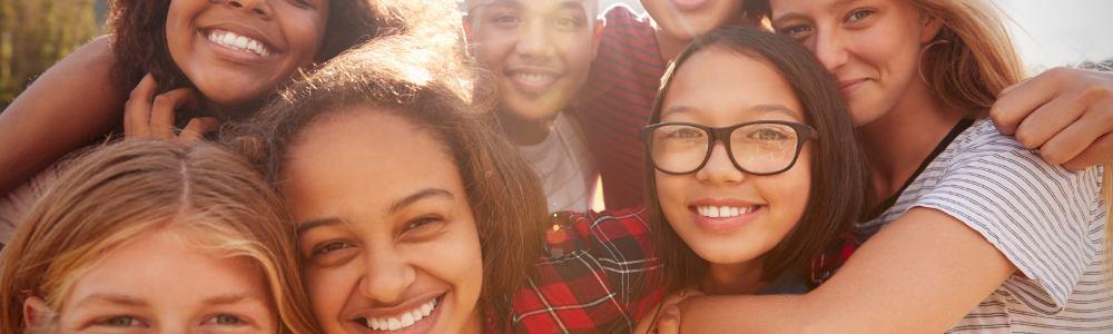 A group of teens on an autumn morning all smiling at the camera happily, on a summer's morning at camp.  