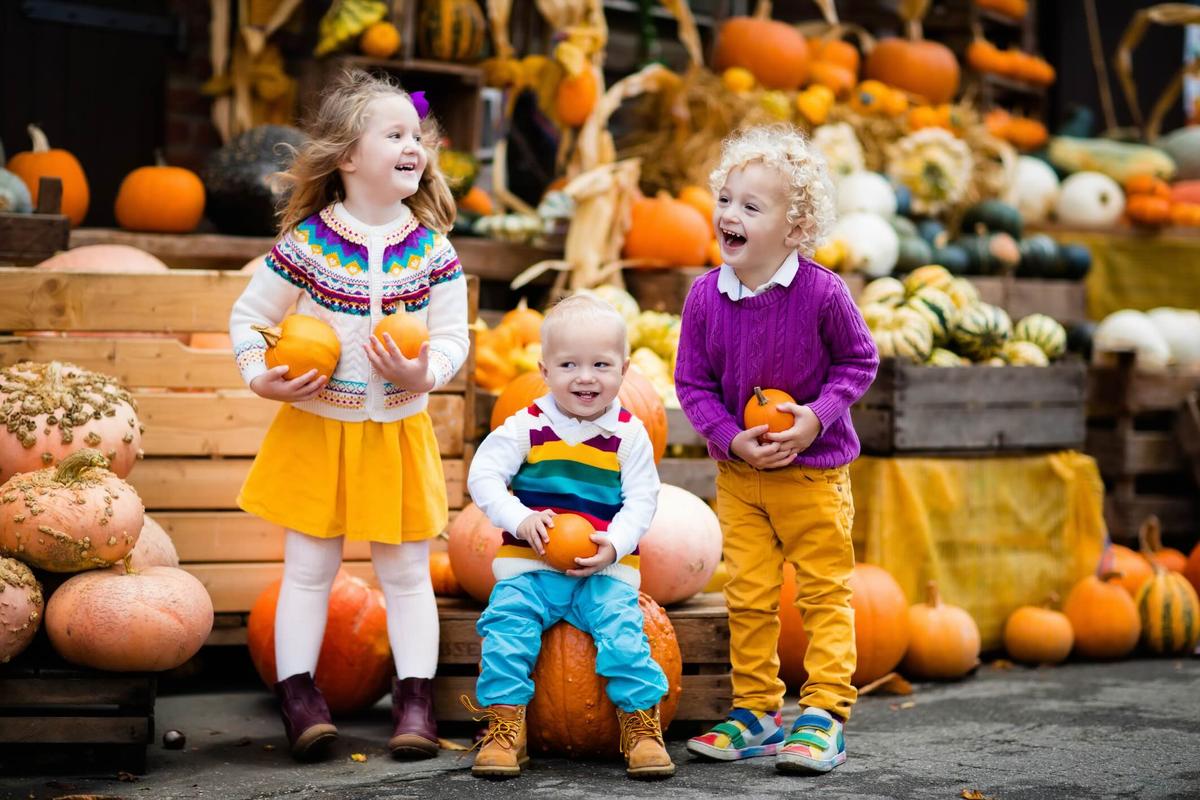 A group of 3 children holding and sitting on a large pumpkin at the pumpkin patch in Juckerhof Seegreben