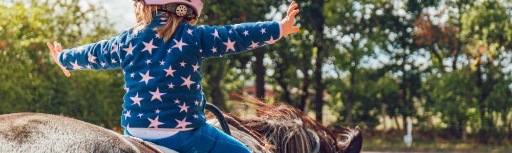 A photo of a girl with a pink helmet finding her balance on a pony at the therapeutic center Magic Garden in Rafina, in Greece.  S