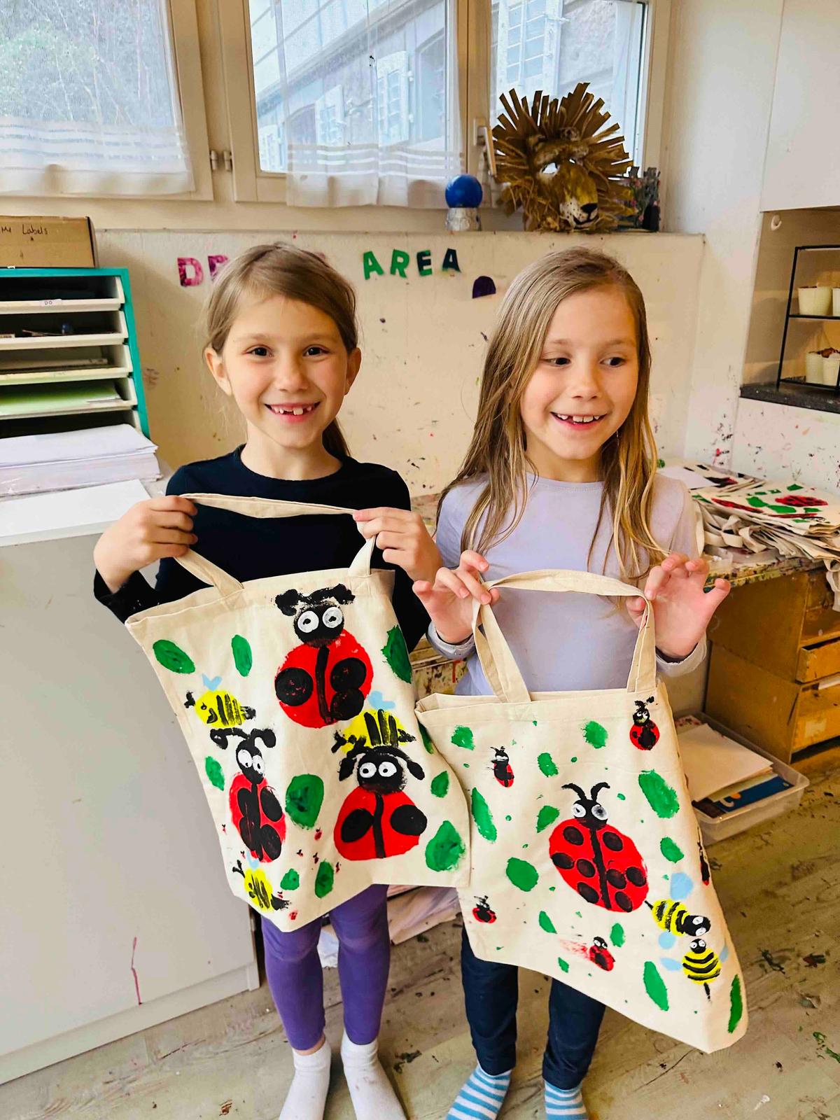 Two girls showing their hand-crafted bags, with painted lady bugs at the Storycraft studio in Rüschlikon, Zurich.  