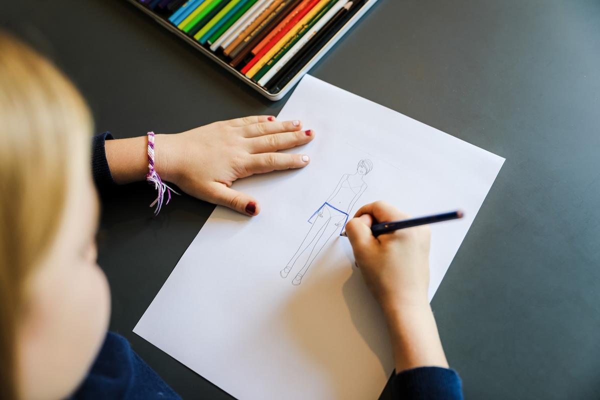 A pair of manicured teenage hands are sketching a skirt design on a model on a piece of paper.  The first step in fashion design at Allegra Fashion Design Winter Camp 2025 in Zollikon.