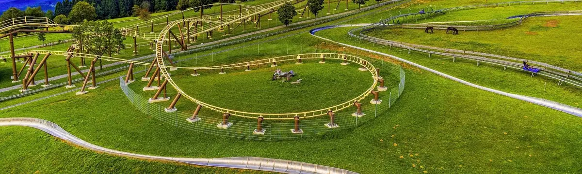 Child riding down the Brunni summer toboggan run on a winding metal track surrounded by green alpine meadows and mountain scenery.