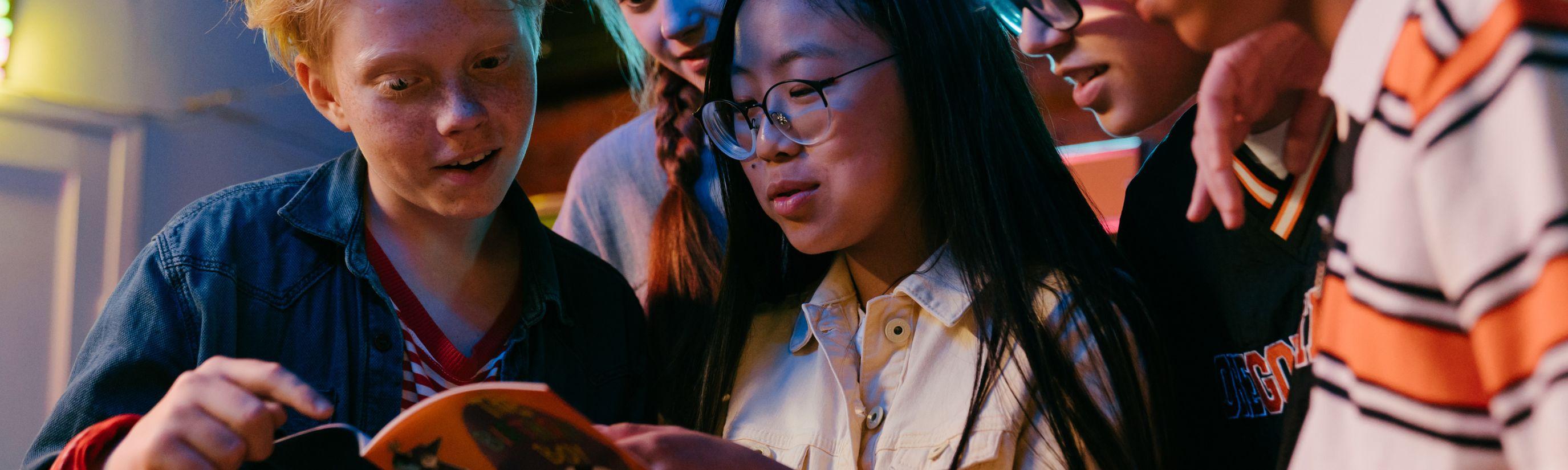 A group of international teens huddling together over a very interesting book.  