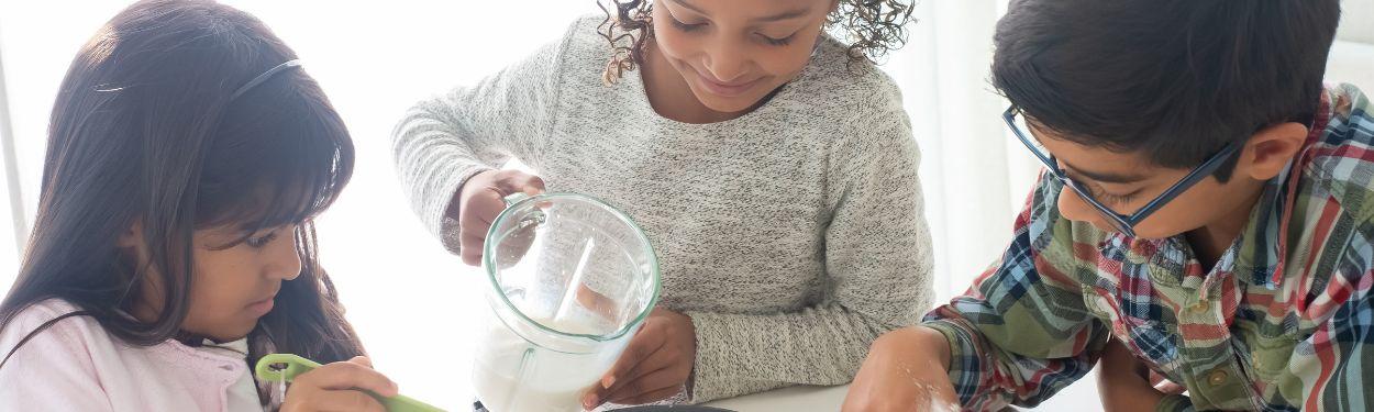 A group of 2 pre-teen girls and 1 pre-teen boy working together to make something to eat together in the kitchen, while learning to measure, to mix and prepare a meal.  