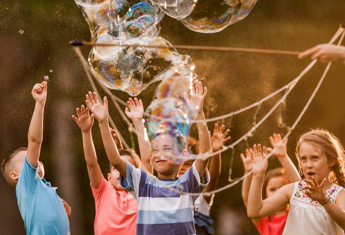 A group of children enjoying giant bubbles in a birthday party outdoors, organized by Elena Simic in Switzerland.  