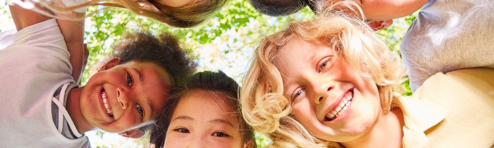 School children juddled-up in a circle smiling at a camera on the ground, after a class at English Club Zollikon.  It is summer and sunny outside in Zollikon, Switzerland.