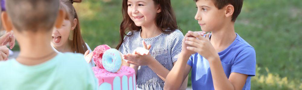 A group of school children celebrating at a children's birthday party at Funmily a playground and family friendly restaurant in Marousi, in Athens, Greece.  The cake is light blue and pink and decorated with donuts.