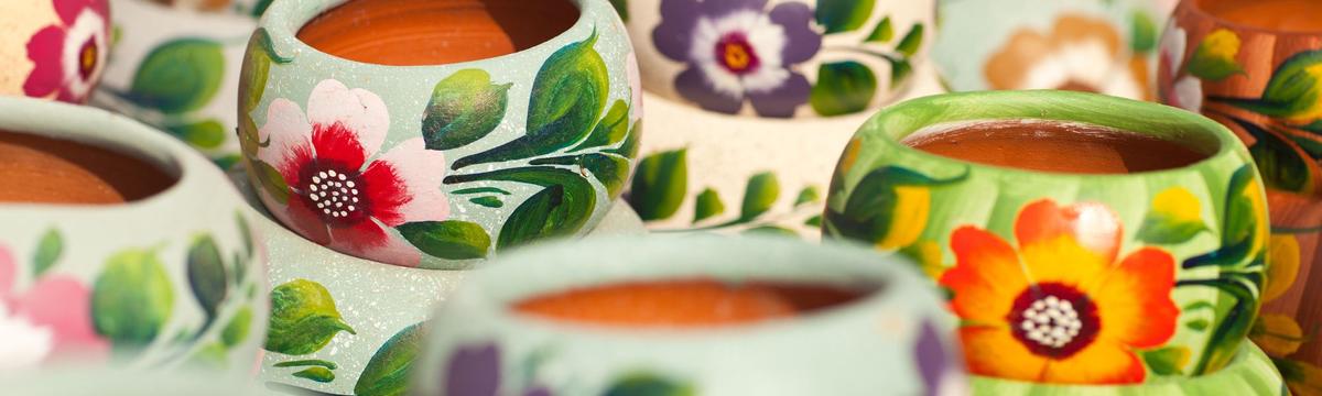 Close-up of colorful hand-painted clay pots, each decorated with vibrant floral patterns in red, orange, purple, and green hues.