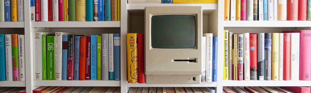 At the Hellenic IT Museum in Athens, children and families can observe the evolution of computer technology through the years, in this case a macintosh computre is on display among some colorful books about informatics on a bookshelf