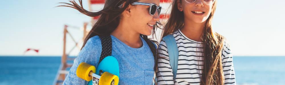 Two pre-teen girls in summer clothes and sunglasses are going skateboard and enjoying the summer sun.