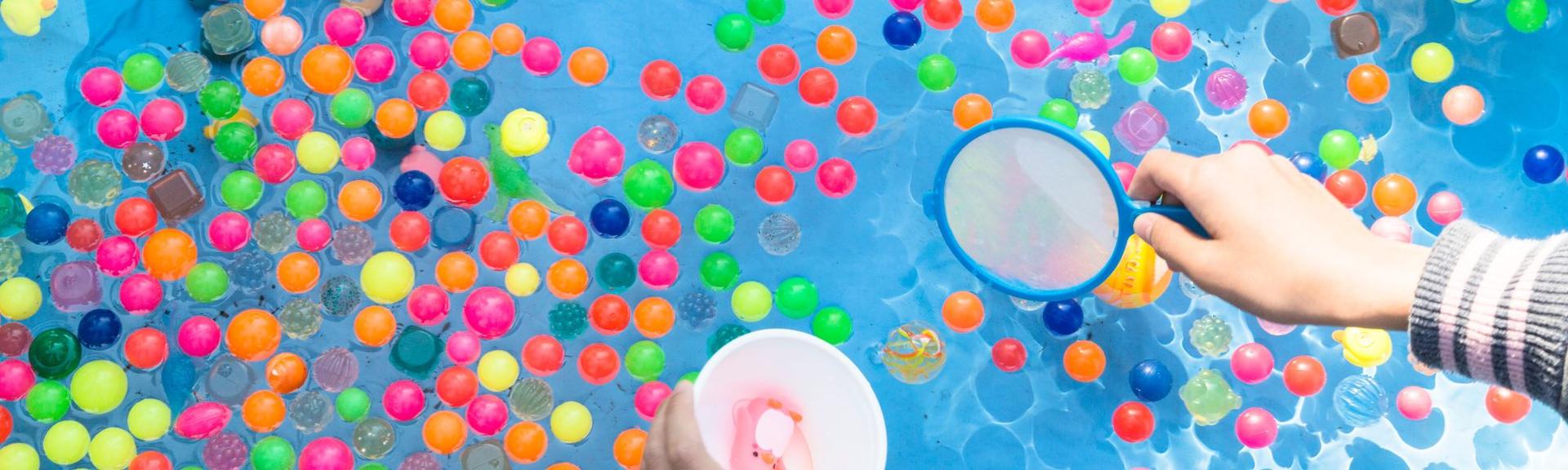 Colorful balls in a blue tank filled with water for kids to play fishing games and STEM exercises by trying to measure the water in the tank and catching balls, while having fun in the garden during the hot summer months.