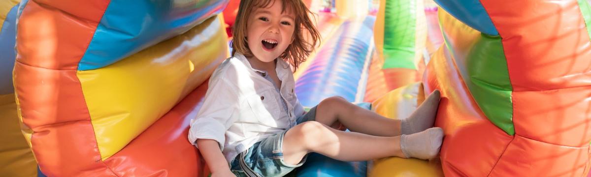 Children sliding inside a colorful bouncy castle on a summer's day at Ta papagalakia playground and creative space in Rentis, Athens, Greece
