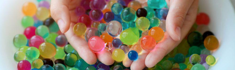 Children's hands dipping into water colorful water beads and scooping-up a hand-full to play and enjoy in the water.  