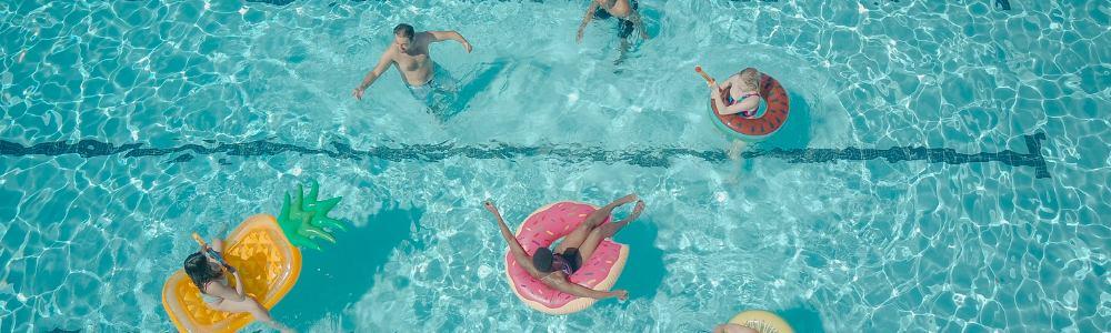 An eagle-view of the pool at Water World in Wallisellen near Zurich, Switzerland.  There are colorful floaties with kids and grown-ups enjoying the swimming pool.  