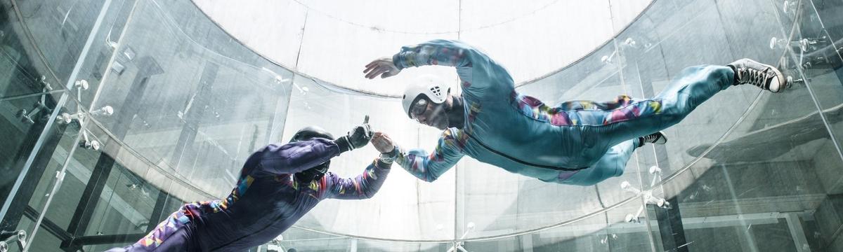 Person floating in a vertical wind tunnel at Windwerk, wearing a flight suit and helmet, experiencing indoor skydiving in a glass-enclosed chamber.