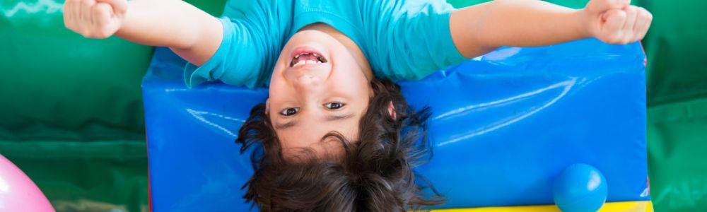 A 6-year old boy facing the camera upside on a blue indoor playground mattress at the indoor playground Barefoot Giants, or Xipoliti Gigades, in Holargos, Greece.