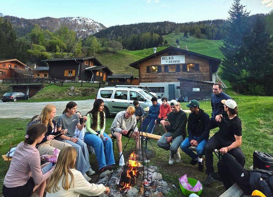 A group of teens around a campfire on a mountain top in Switzerland, organized by language camp provider frilingue.