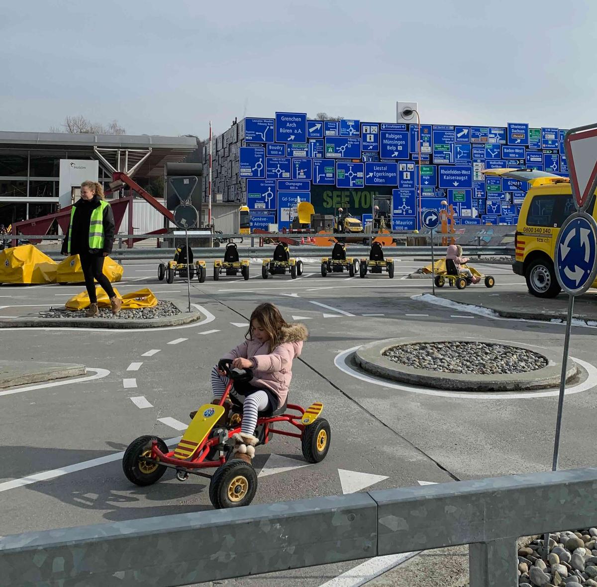 Children driving through a special outdoor circuit with pedal carts, discovering road indicators and signs at the Luzern Transport Museum, Switzerland.