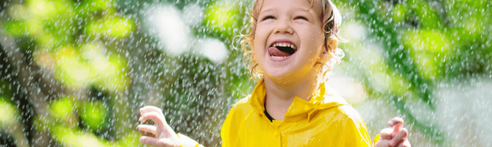 A girl in a yellow raincoat is enjoying an autumn rain shower in Zurich, Switzerland by getting wet and tasting the raindrops falling on her face.