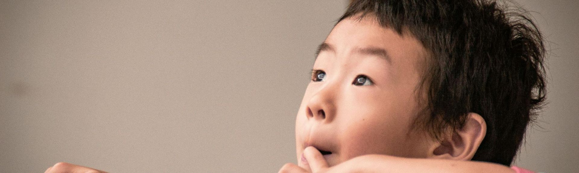 A school-aged asian boy looking up towards the sky wondering and thinking about something he is curious about.  