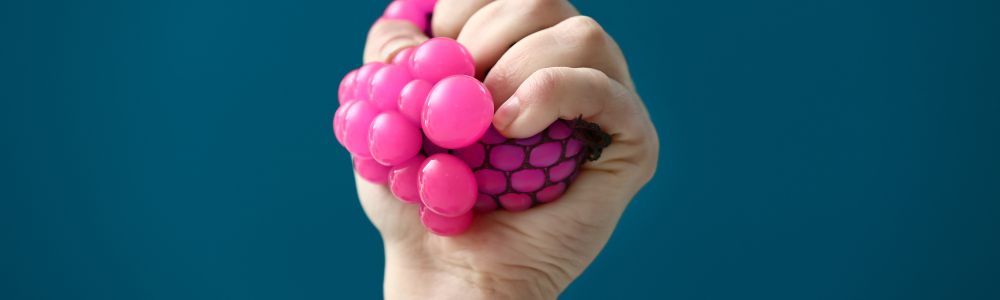 A child's hand squeezing a bright pink stress ball from his quiet box, a box where children and parents can keep fun distractions that help them release tension that is hard to express with words, as described in the blog post Create Your Own 'Calm Down Box': A Small Tool for Big Emotional Moments on Momizen.