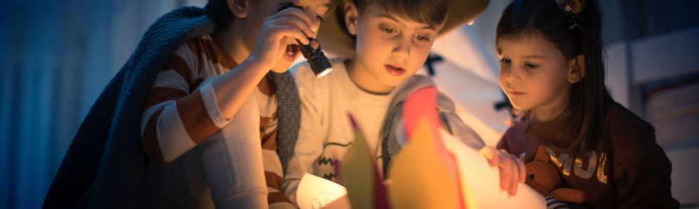 Three kids shining light on a home-made map they made to search for treasures at home during an evening without screens and tablets