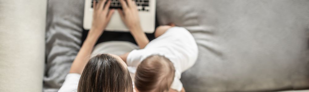 Swiss mom on her laptop and with her baby in her arms, trying to get admin work done at home, under pressure.  
