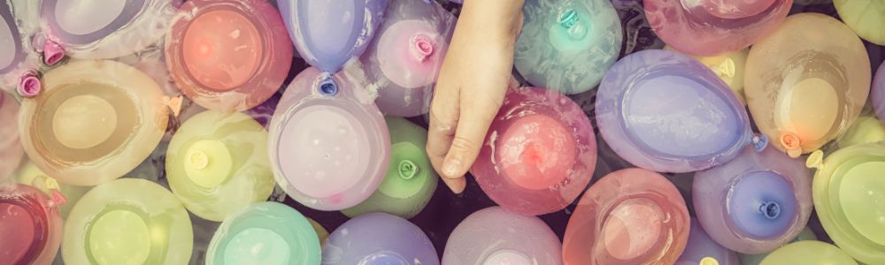 A child's hand dipping into a large bucket filled with water balloons and water, ready to play and perform sun experiments on a summer afternoon.  