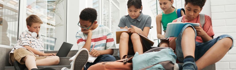 A group of teens sitting together on the floor and bean-bags doing their homework and working on a project all together.  They come from different coutries and nationalities and are focused on education and personal development. 