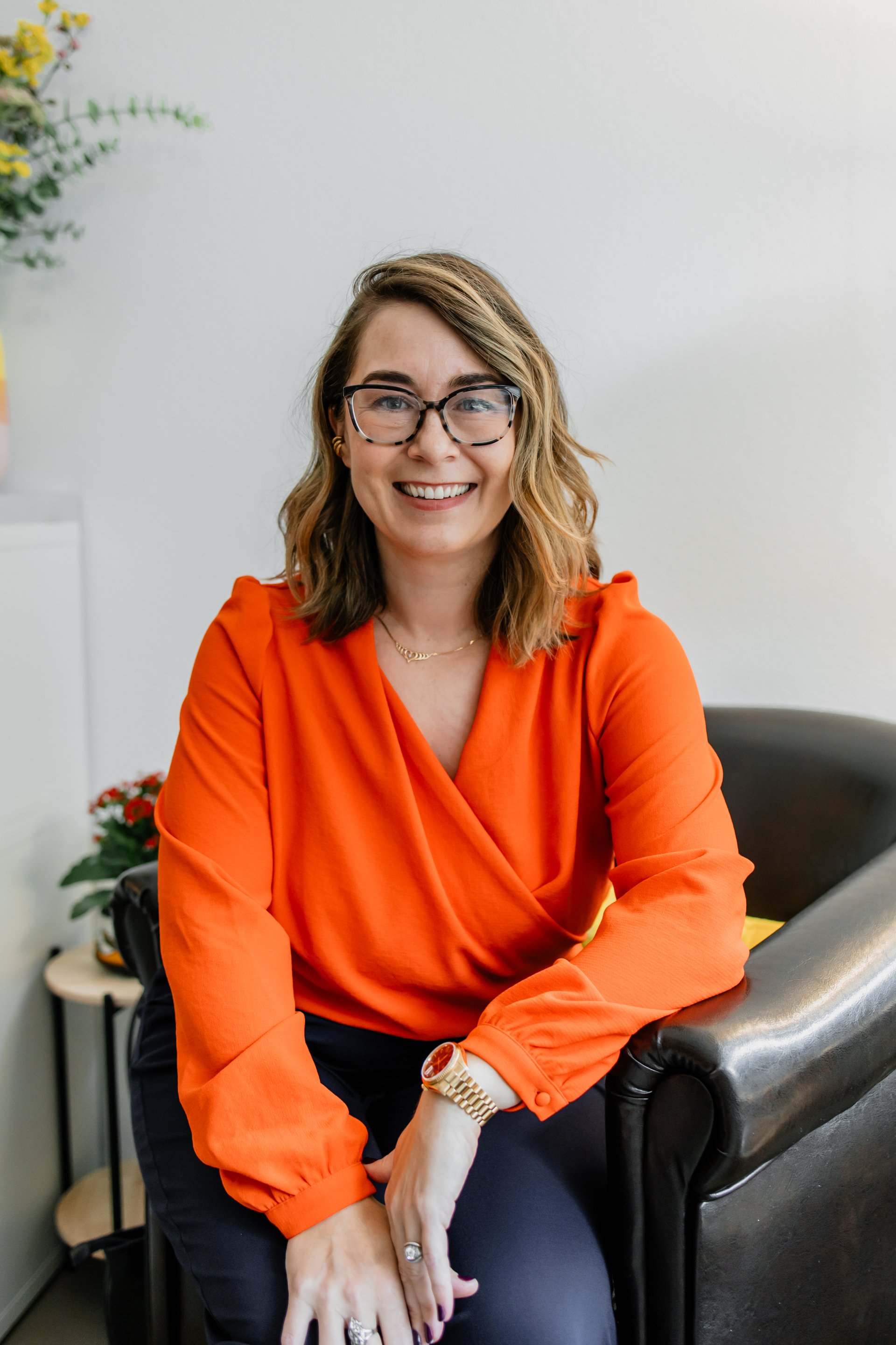 Kristine, founder of Compassionate wearing a bright orange shirt in a profile shot.  